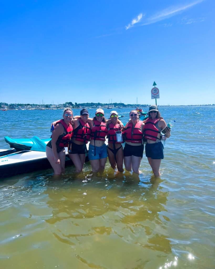 Group of people in life jackets at the beach with jet skis.