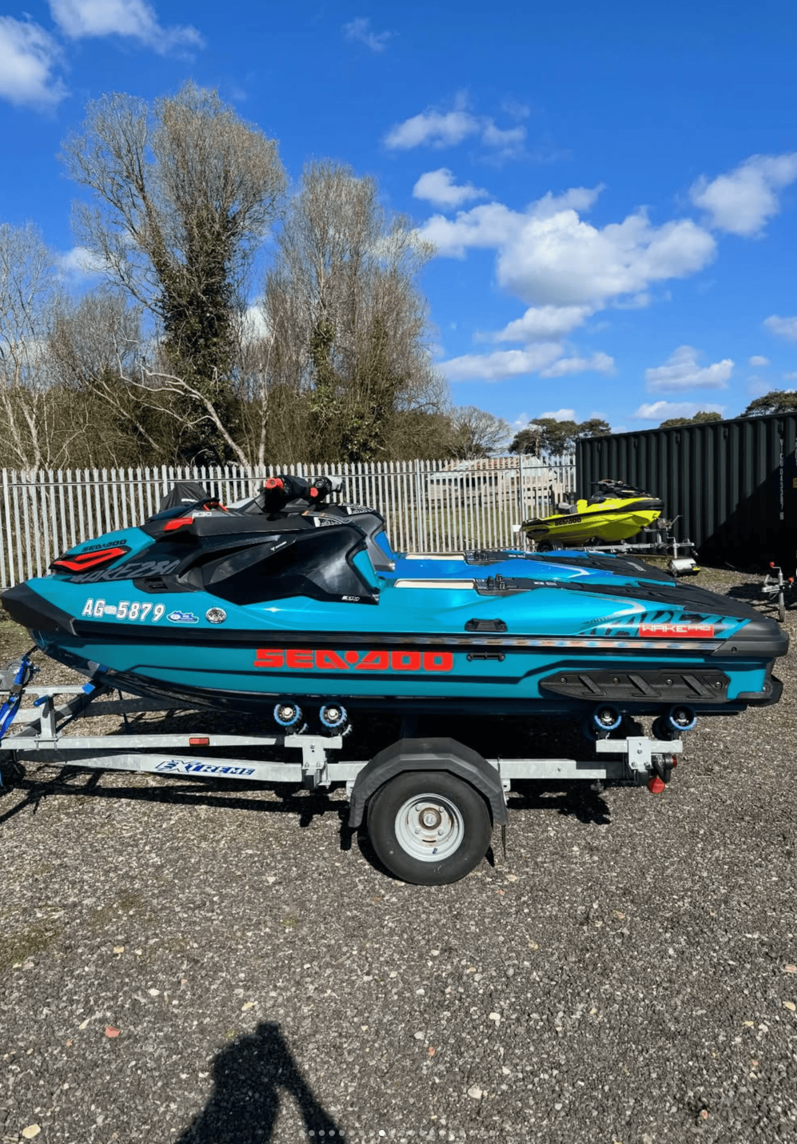 Blue Sea-Doo jet ski on trailer at marine site with trees and sky in background.